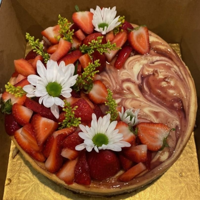 A strawberry swirl cheesecake from Crumble & Whisk, topped with fresh strawberries and white daisies.