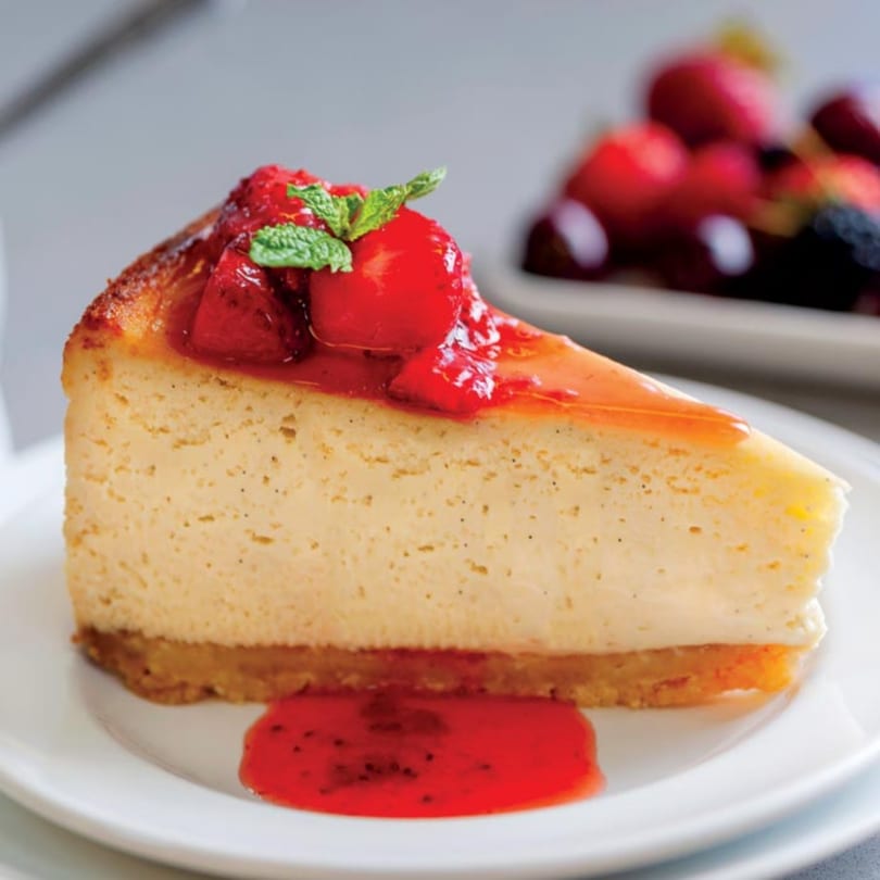 A slice of Crumble & Whisk cheesecake with strawberry topping and mint garnish on a white plate.