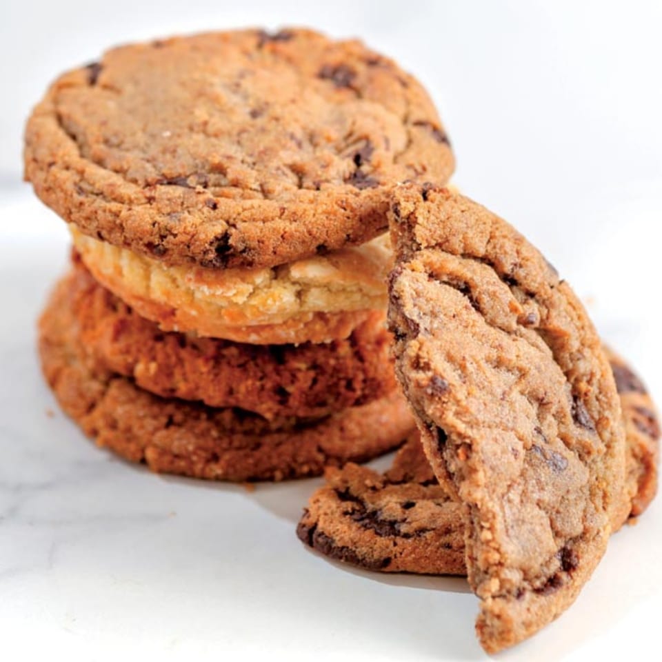 A stack of Crumble & Whisk chocolate chip cookies with one leaning against the stack.