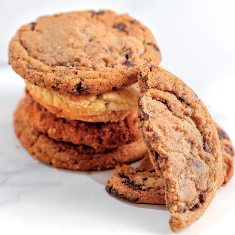 A stack of Crumble & Whisk chocolate chip cookies with one leaning against the stack.