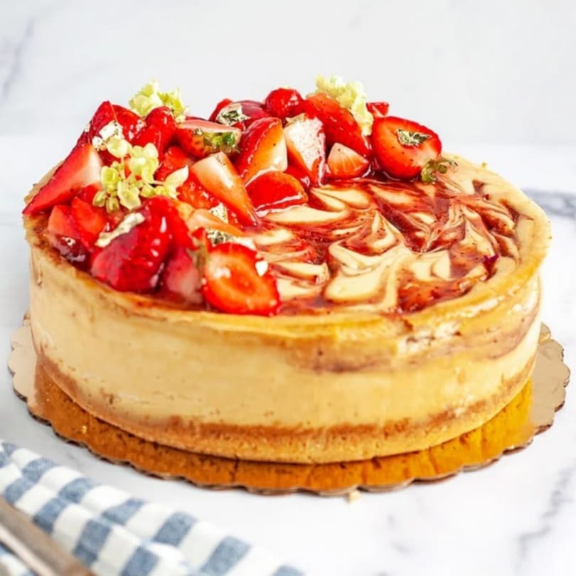 Crumble & Whisk strawberry cheesecake with a swirled top, garnished with fresh strawberries and edible gold.